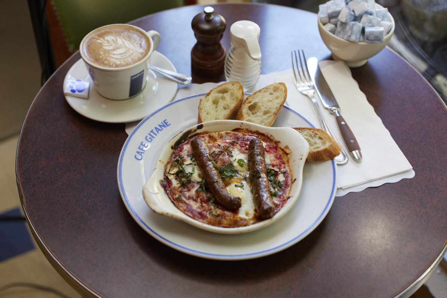 Merguez sausages on a spiced base with bread, beside a cappuccino
