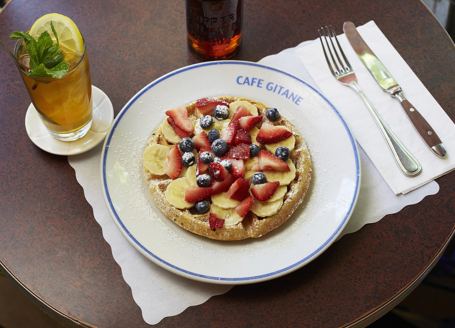 A fruit tart topped with strawberries and blueberries on a Cafe Gitane plate