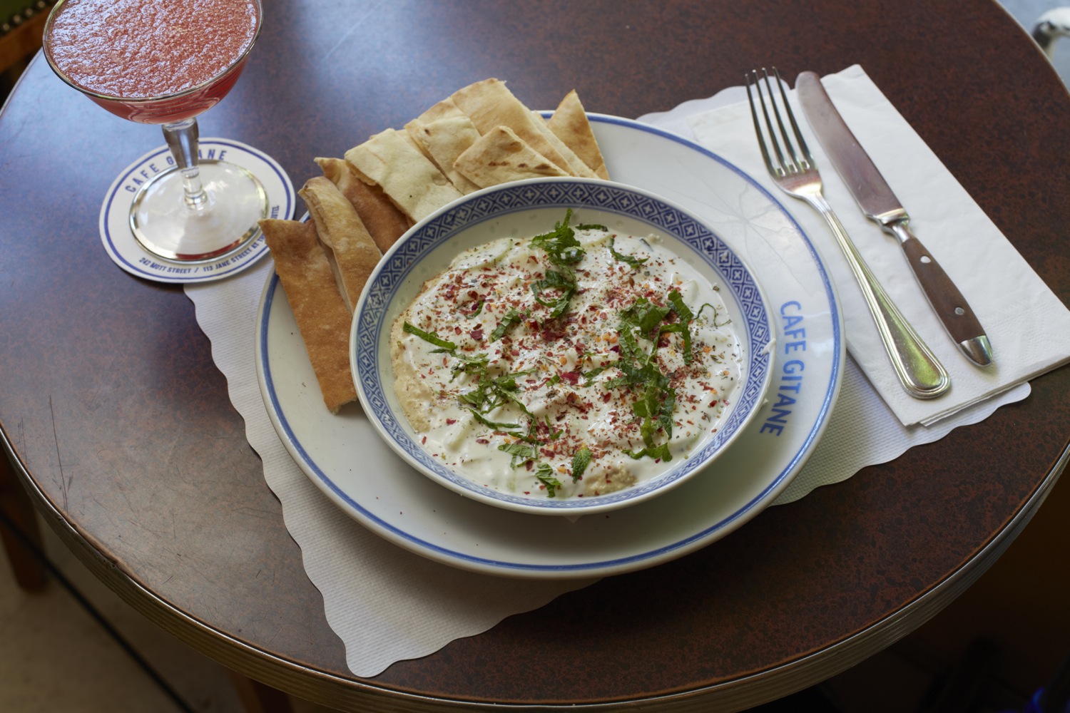 A herbed dip in a bowl with flatbread and a cold pink drink