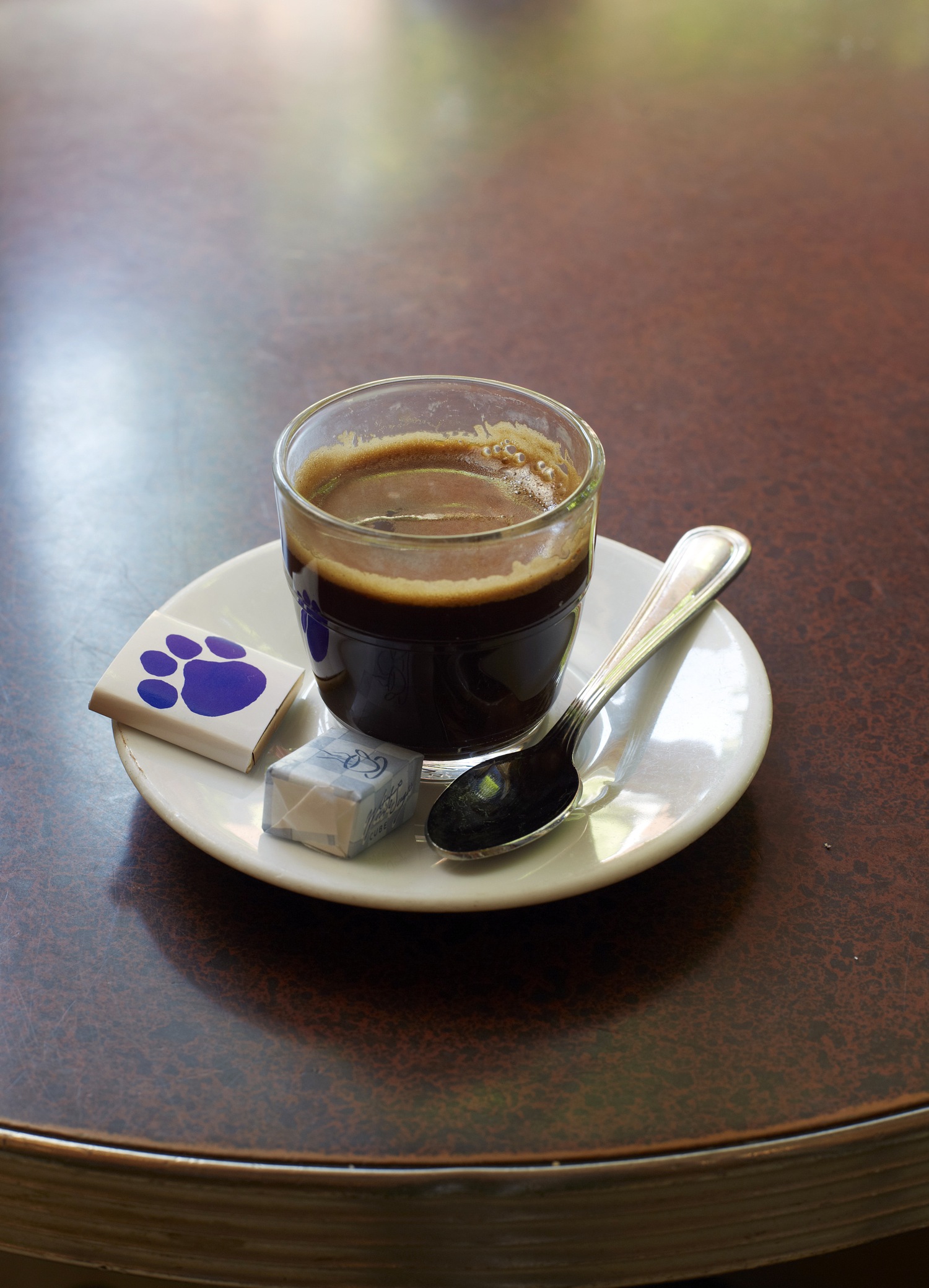 An espresso in a small cup and saucer on a dark cafe table