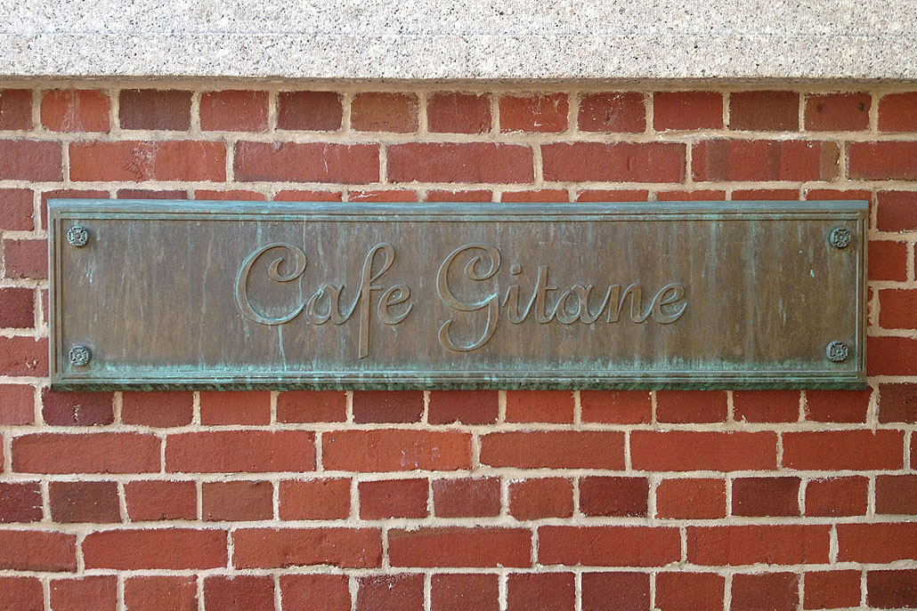 A weathered brass Cafe Gitane plaque mounted on a red brick wall