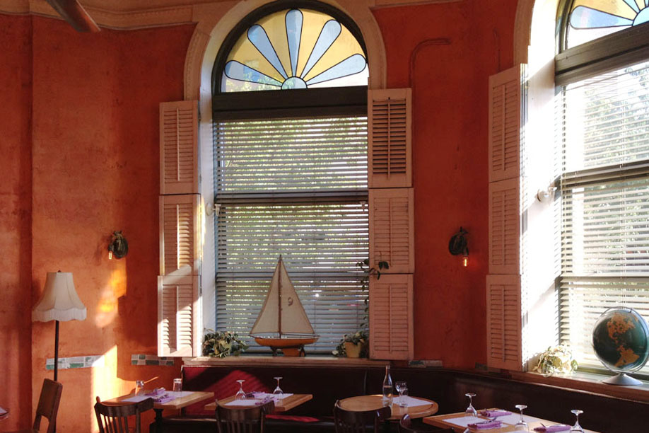 An arched window in a terracotta-walled dining room with a model sailboat on the sill
