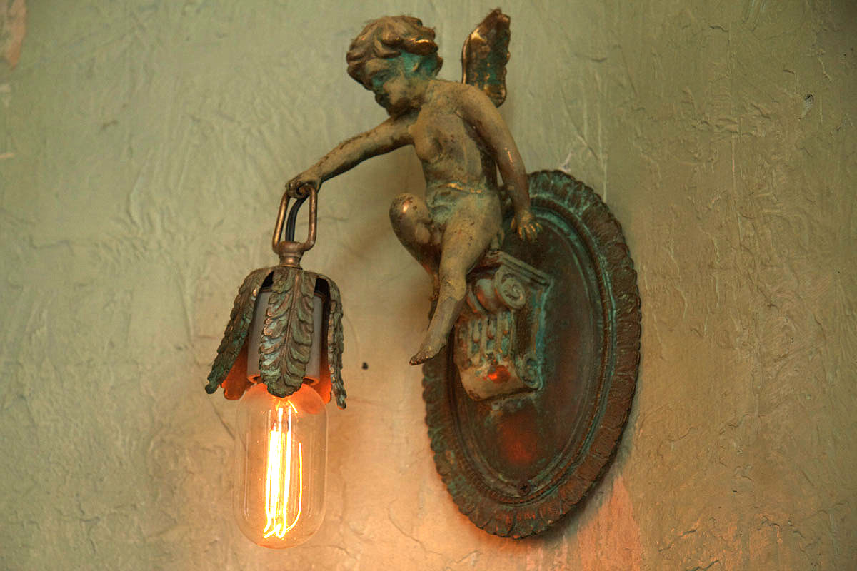 A cherub wall sconce holding an exposed filament bulb