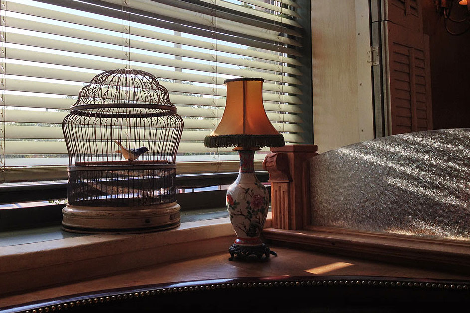 A birdcage and a table lamp on a windowsill above a banquette