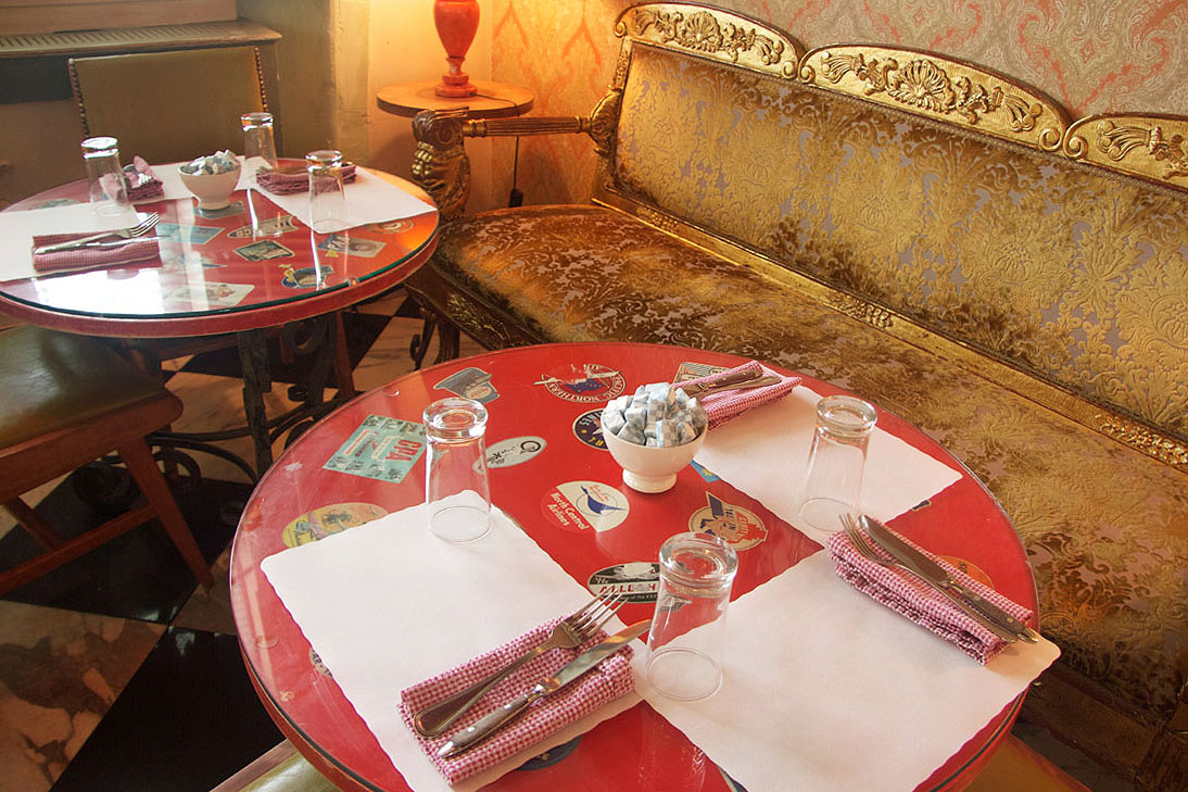 A red cafe table laid with cutlery beside a gilded banquette