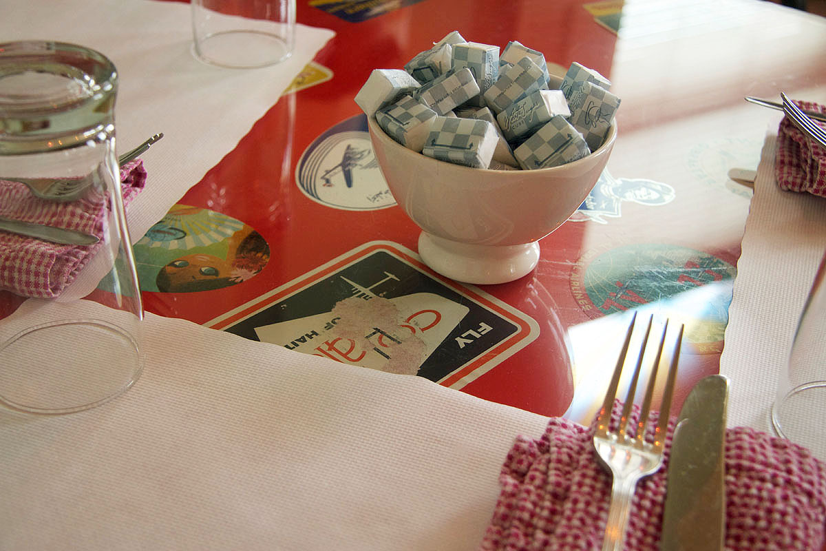 A table setting with a sugar bowl and checked napkin on a red tabletop
