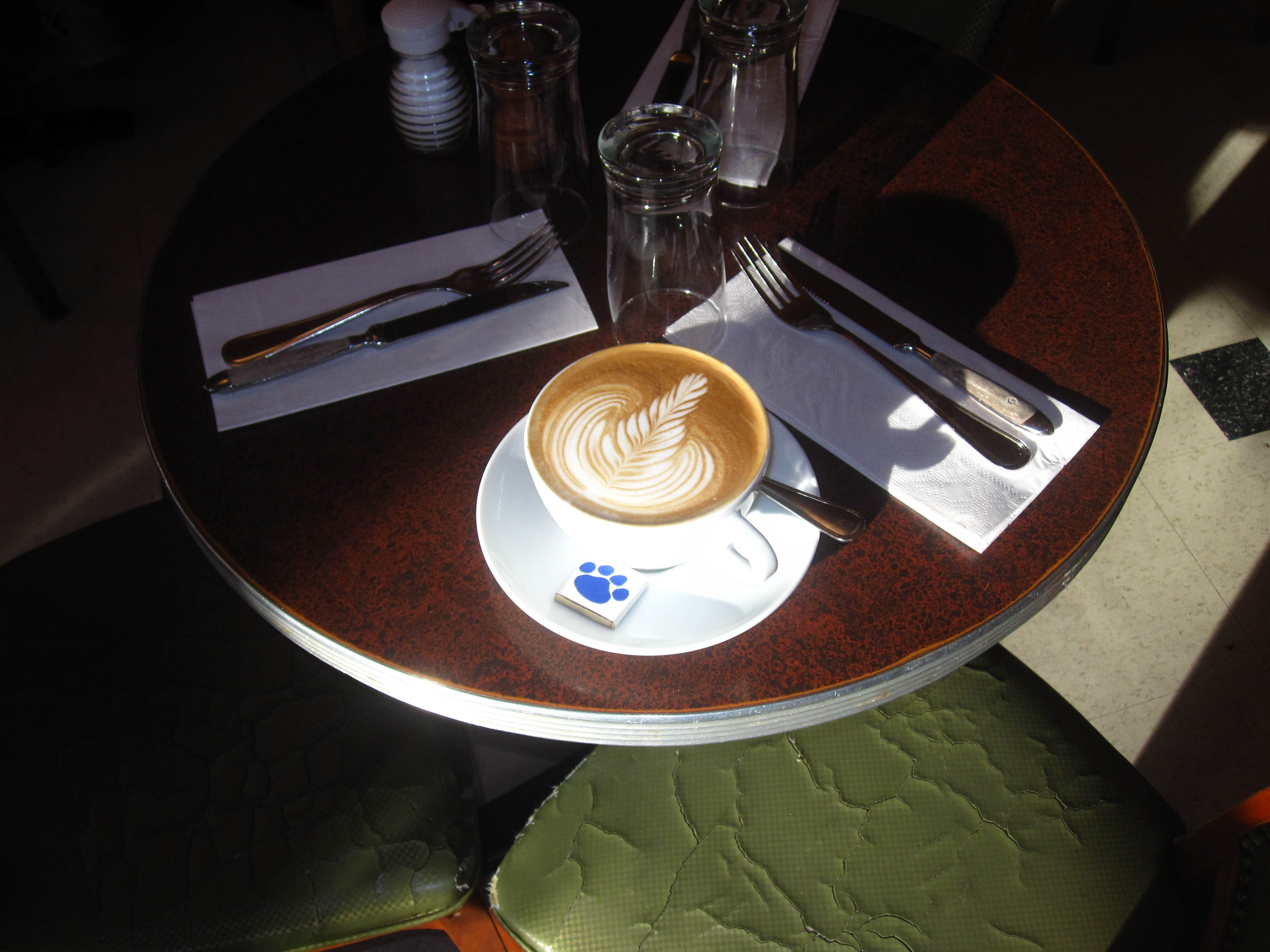 A cappuccino with latte art on a dark round table beside a green banquette