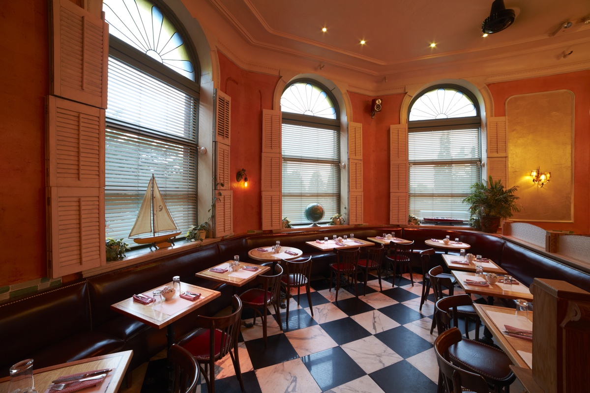 A dining room with checkerboard tiling, arched windows and dark banquettes